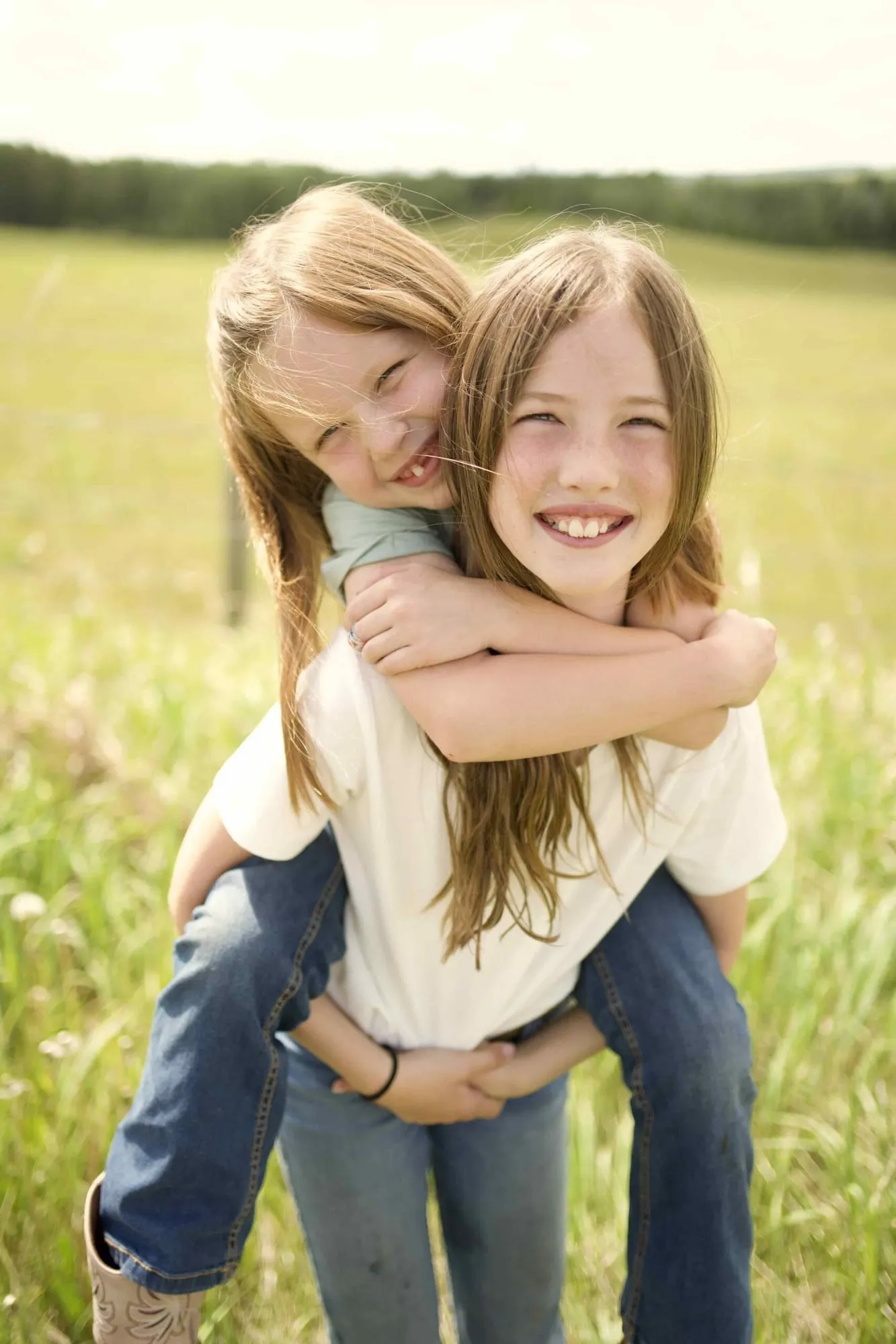 Two sisters laughing during a piggyback ride in a summer field