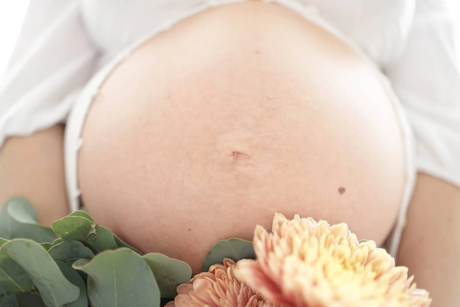 Pregnant belly framed by dahlias and greenery