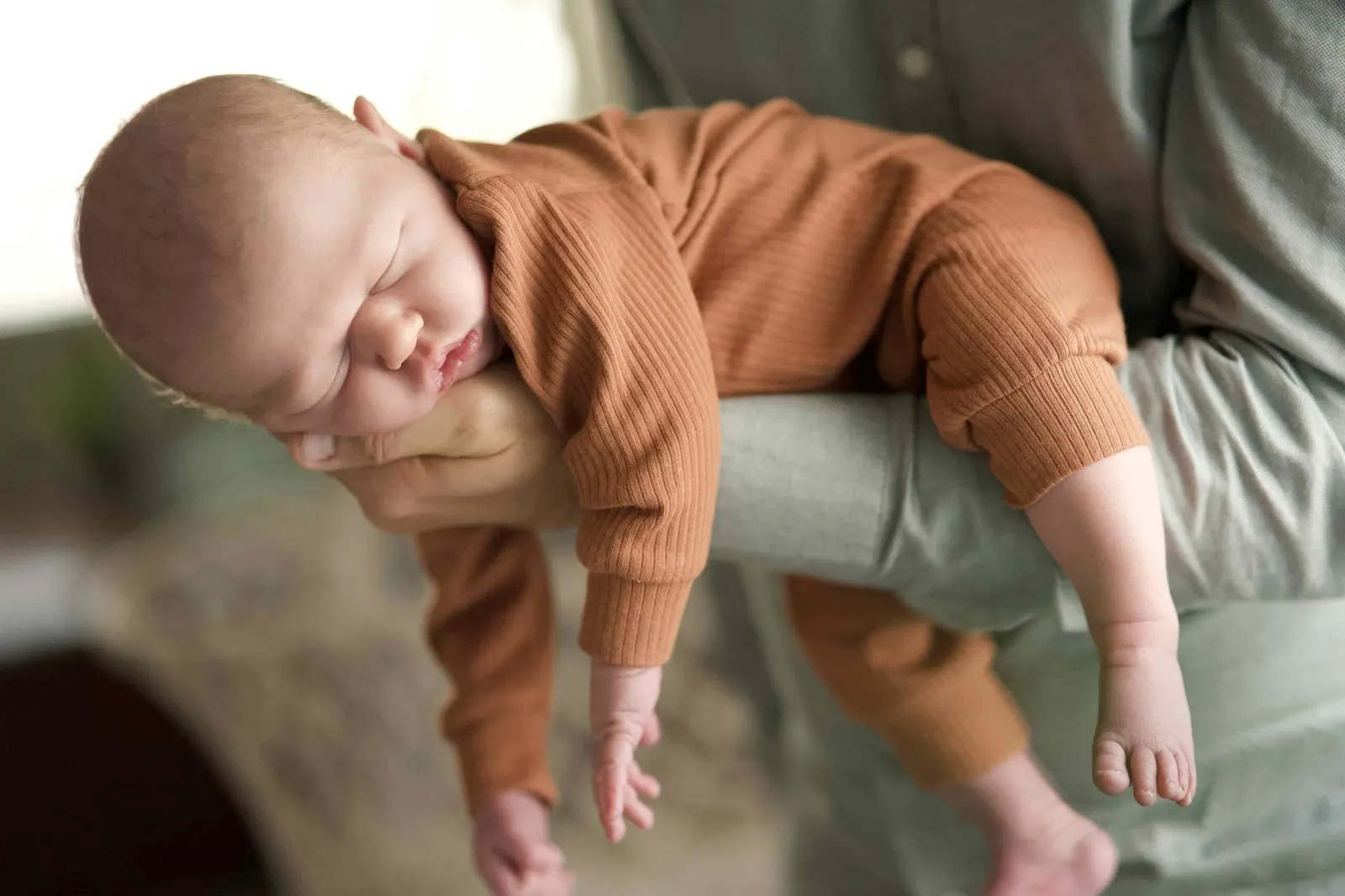 Sleeping baby in a rust knit outfit draped over a parent's arm