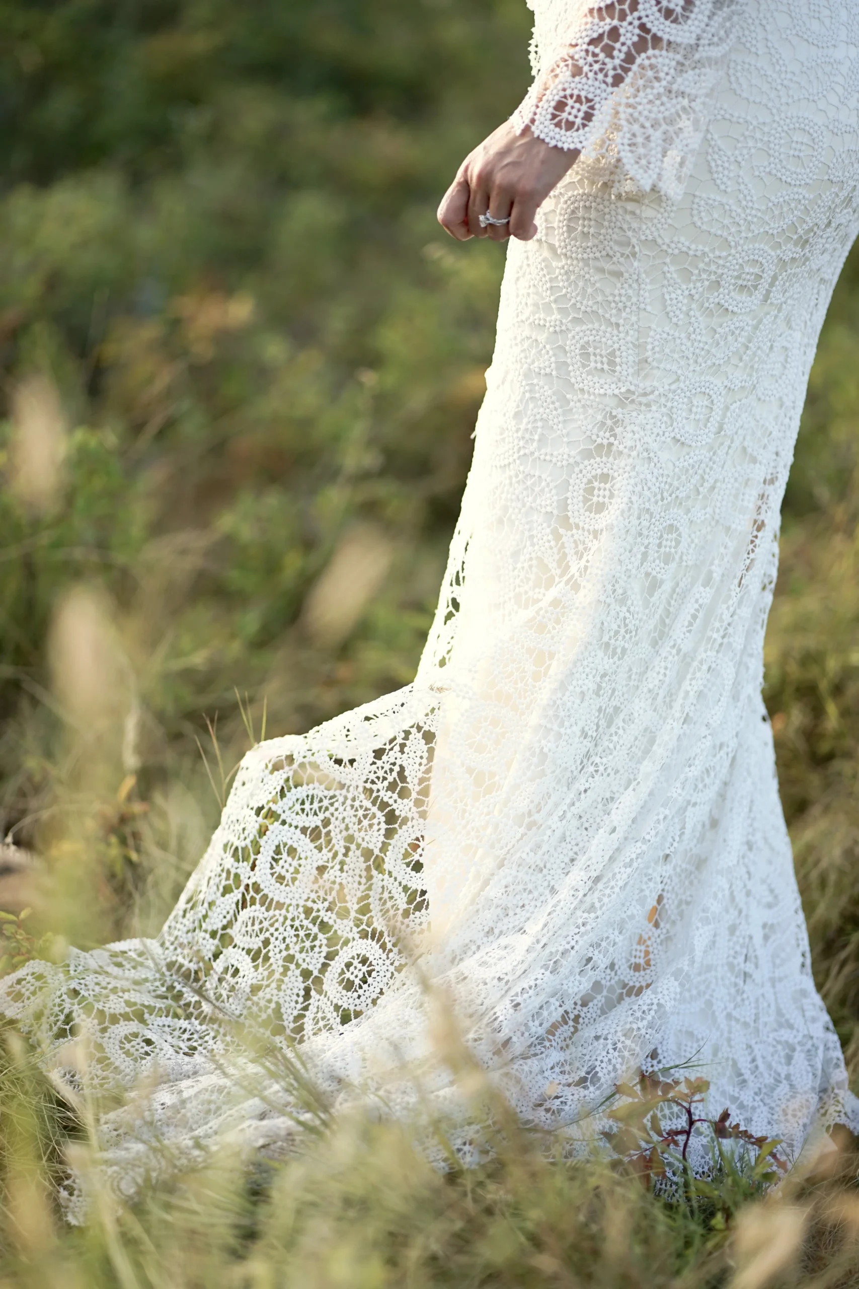 Detail of a lace wedding gown train laid in a grassy field, from a Calgary wedding photography session
