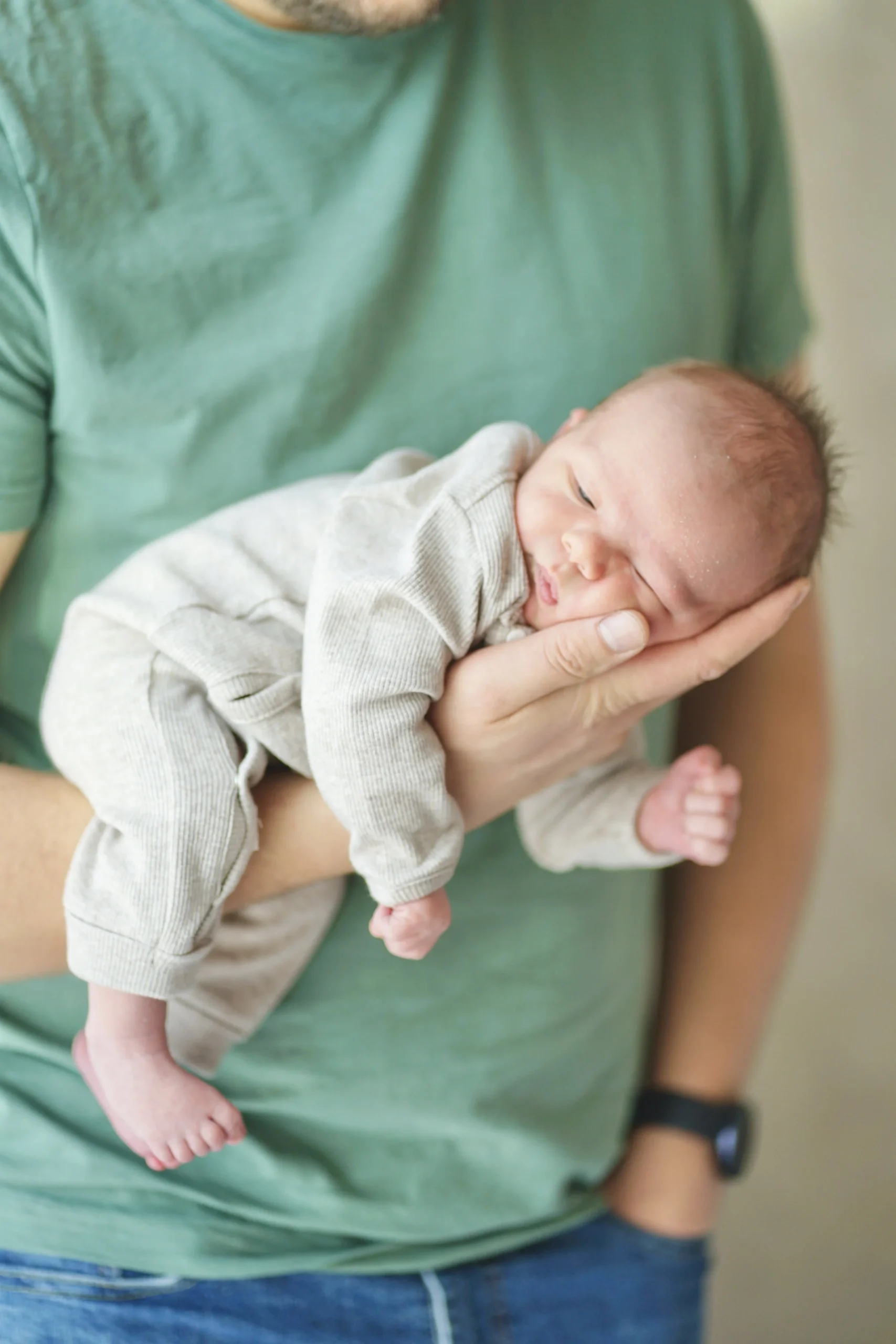 Newborn baby cradled gently in a parent's arm, wrapped in soft beige layers