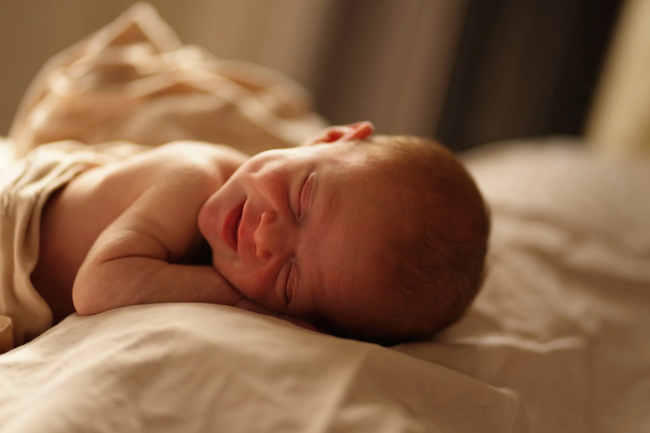 Close-up of a sleeping newborn baby with soft red hair, lit by warm golden light