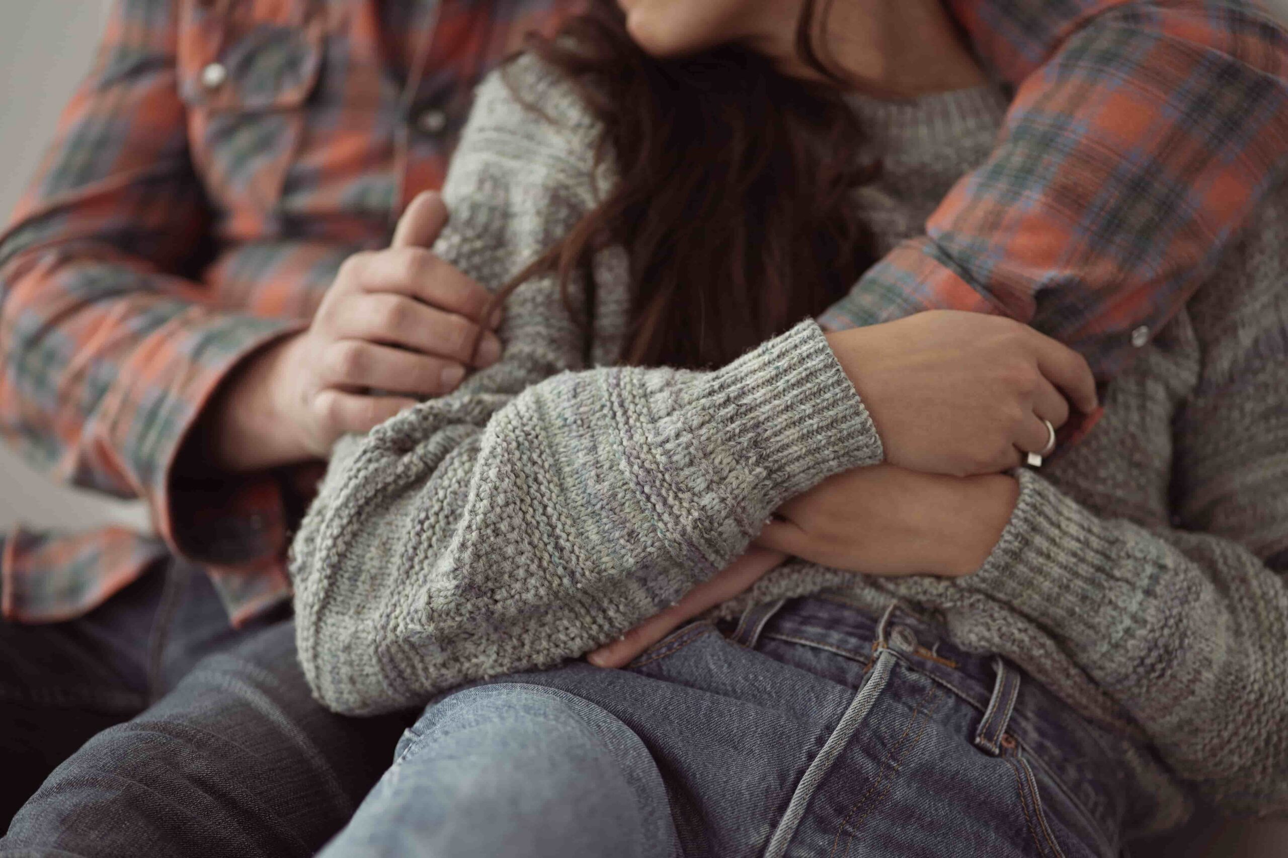 Couple embracing closely, one in a plaid shirt and the other in a knit sweater