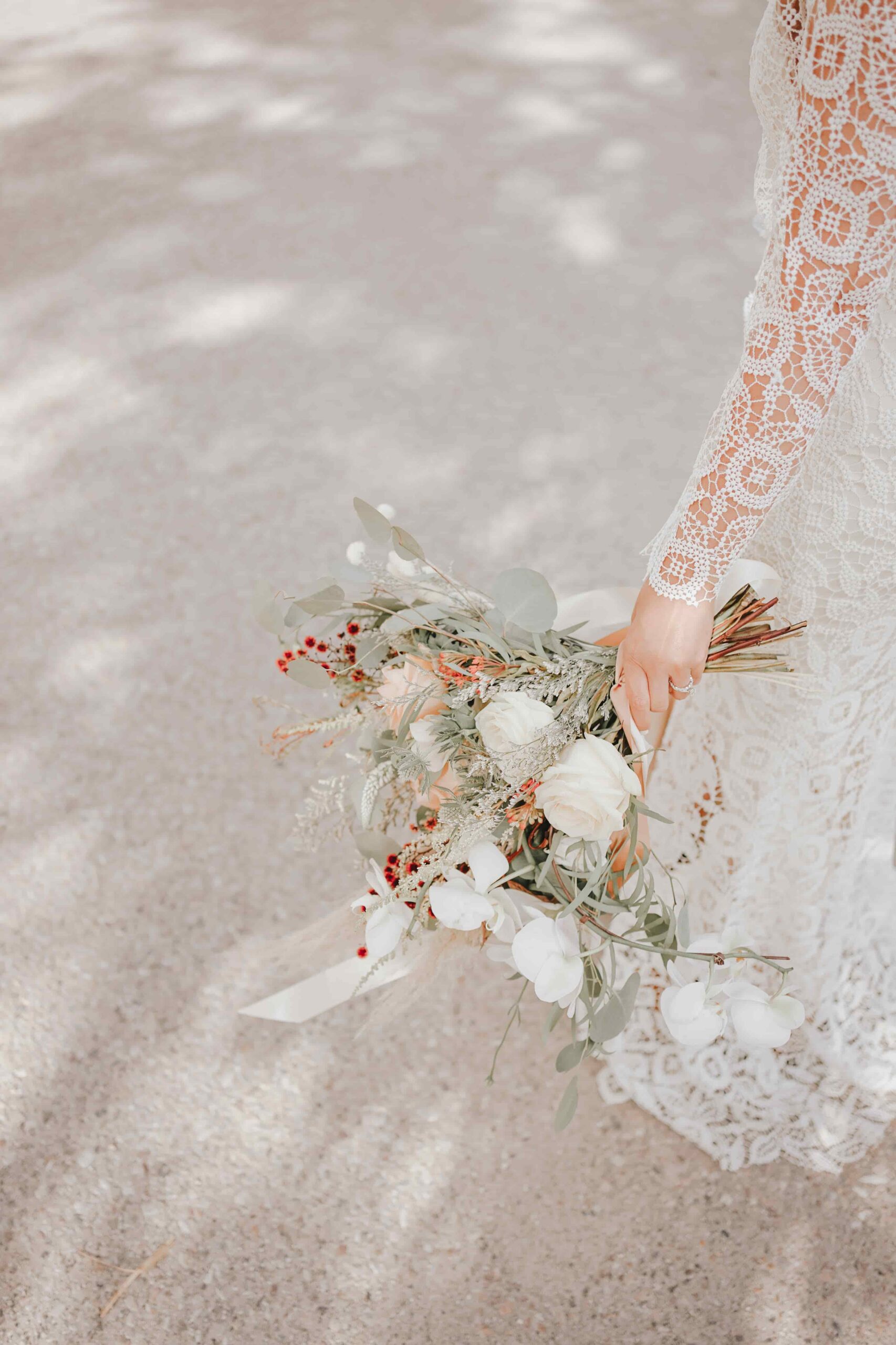 Dried wildflower bridal bouquet with a trailing lace ribbon resting on sand